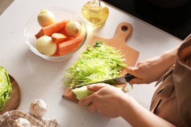 Genç bir kadın mutfakta ahşap tahtada lezzetli borş için lahana kesiyor.