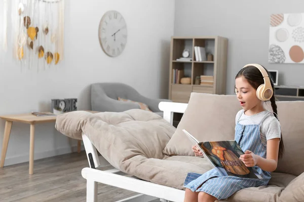 Little Girl Headphones Reading Book While Sitting Sofa — Stock Photo, Image