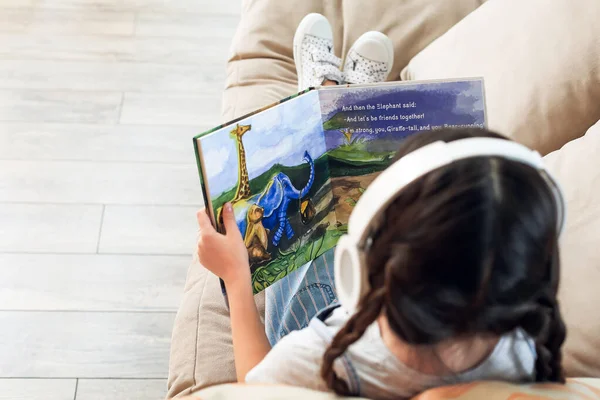 Niña Con Auriculares Libro Lectura Mientras Está Sentado Sofá — Foto de Stock