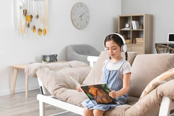 Niña Con Auriculares Libro Lectura Mientras Está Sentado Sofá — Foto de Stock