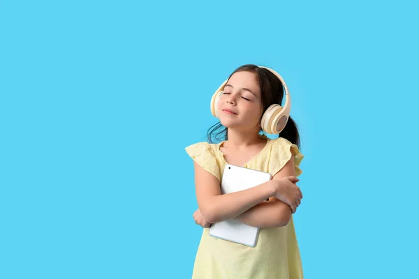 Little girl with tablet computer and headphones on color background