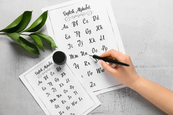 Woman writing English alphabet on light background