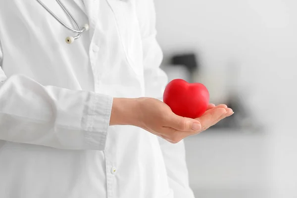 Female cardiologist with red heart on light background, closeup
