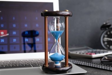 Kum saati ve dizüstü bilgisayar koyu arkaplanda. Son teslim tarihi kavramı