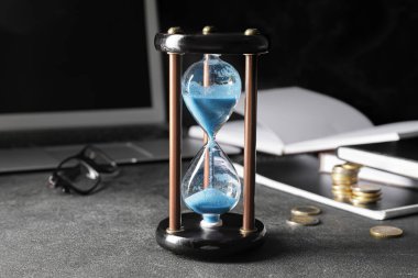 Ofisteki karanlık masada kum saati ve dizüstü bilgisayar. Son teslim tarihi kavramı