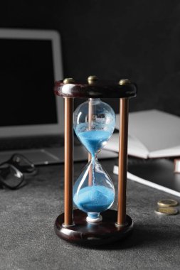 Ofisteki karanlık masada kum saati ve dizüstü bilgisayar. Son teslim tarihi kavramı