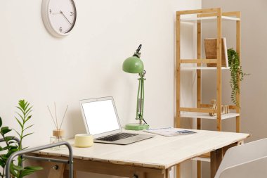 Işık duvarının yanında dizüstü bilgisayarı, lambası ve dekoru olan modern işyeri