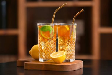 Glasses of tasty ice tea with lemon on table in room clipart