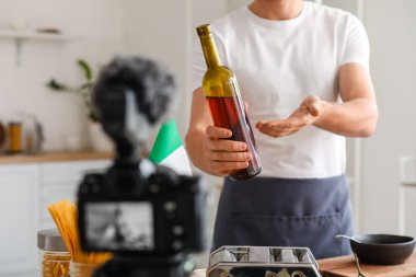 İtalyan aşçı elinde şarap şişesiyle mutfakta video kaydı yapıyor.