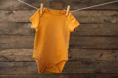 Bebek giysileri ahşap arka planda ipte sallanıyor.