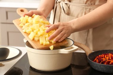 Mutfaktaki tencereye patates ekleyen kadın.