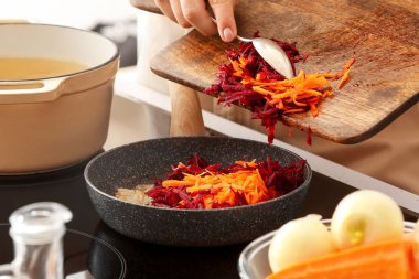 Mutfaktaki tavaya rendelenmiş havuç ve pancar koyan kadın, yakın plan.