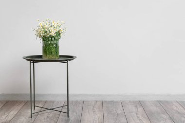 Lamba duvarının yanındaki masada papatya çayı olan vazo.