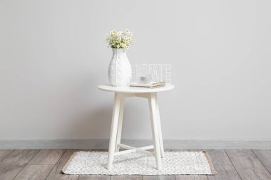 Lamba duvarının yanındaki masa üzerinde papatya ve dekor olan vazo.