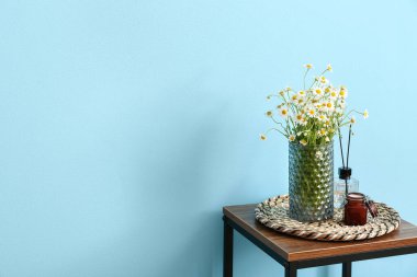 Vazo papatya ve kamış ayırıcı renkli duvarın yanındaki masada.