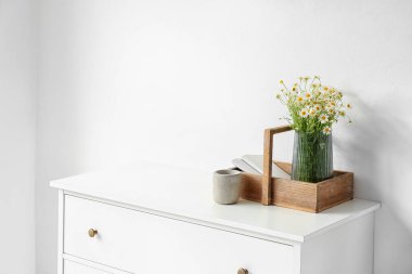 Papatya ve mum dolu sepet, ışık duvarının yanında.