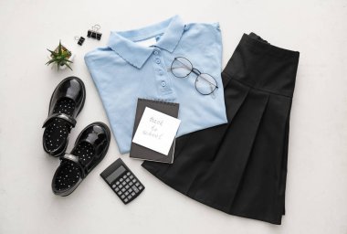 Şık okul üniforması, kırtasiye malzemesi, gözlük ve kağıt çarşaf. Açık arkaplanda okula dönüş metni.