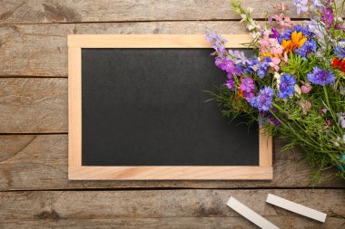 Boş karatahta, bir buket güzel çiçek ve tahta zemin üzerinde tebeşir.