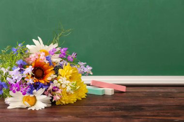 Bir buket güzel çiçek ve sınıftaki ahşap masa üzerindeki tebeşir.