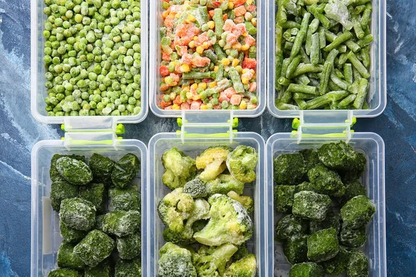 Plastic containers with different frozen vegetables on color background