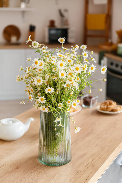 Vase with chamomiles on table in kitchen