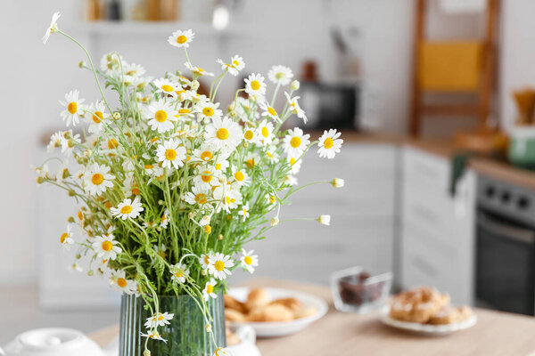 Vase with chamomiles on table in kitchen