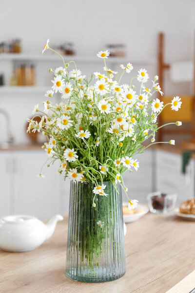 Vase with chamomiles on table in kitchen