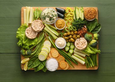 Farklı yeşil sebzeli pano ve ahşap arka planda soslu kaseler.