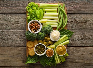 Farklı yeşil sebzeler ve ahşap zemin üzerinde sos olan kaseler.