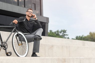 Bisikletli bir işadamı şehir caddesinde cep telefonuyla konuşuyor.