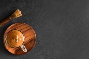 Bir bardak lezzetli dalgona hojicha latte ve koyu arkaplanda chasen.