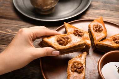 Ahşap arka planda, lezzetli baklavaları tabaktan alan kadın, yakın plan.