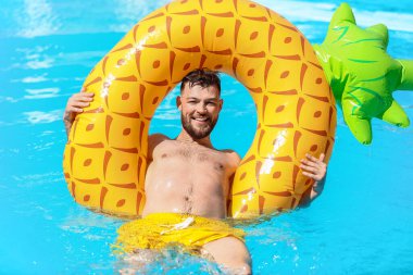 Yüzme havuzunda şişme yüzüğü olan genç bir adam.