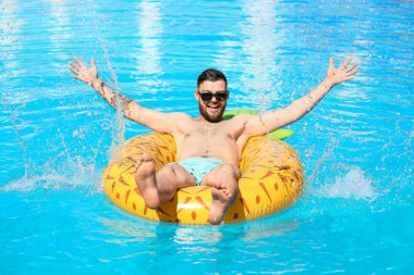 Yüzme havuzunda şişme yüzüğü olan genç bir adam.
