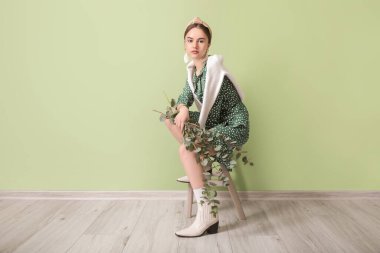 Renk duvarının yanında okaliptüs dalları olan güzel genç bir kadın.