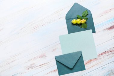 Zarflı boş kart ve beyaz ahşap arka planda güller.