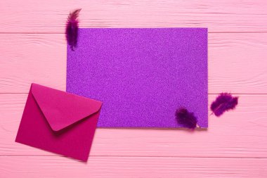 Zarflı boş kart ve pembe ahşap arka planda tüyler