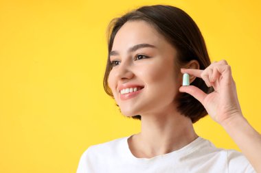 Sarı arka planda kulak tıkacı olan genç bir kadın.