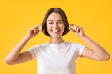 Sarı arka planda kulak tıkacı olan genç bir kadın.