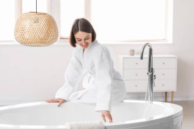 Genç bir kadın sıcak suyla küvet işletiyor.