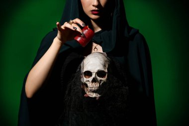 Young witch with skull and candle on dark color background clipart