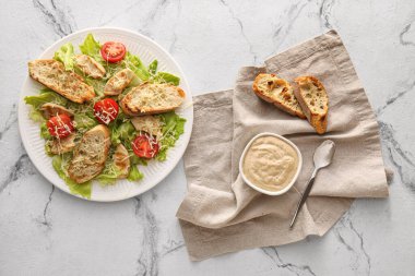 Beyaz mermer zemin üzerinde Sezar salatası ve sos tabağı