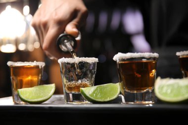 Barmen bardaki masada bardaklara lezzetli tekila dolduruyor.