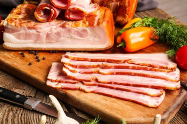 Lezzetli tütsülenmiş domuz pastırması ve ahşap arka planda taze sebzeler.