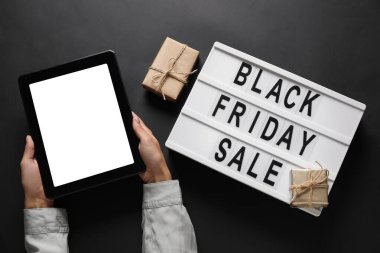 Tablet bilgisayarlı eller, hediyeler ve yazılı pano Koyu arkaplanda Kara Cuma satışı