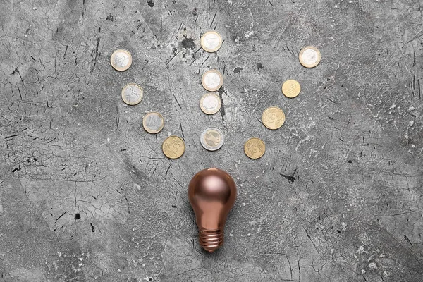 Light bulb with coins on grunge background