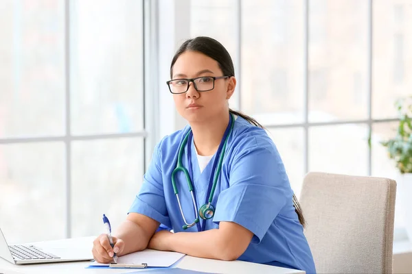 Female Asian doctor sitting at table in clinic