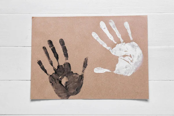 Paper with different handprints on white wooden background. Concept of racism