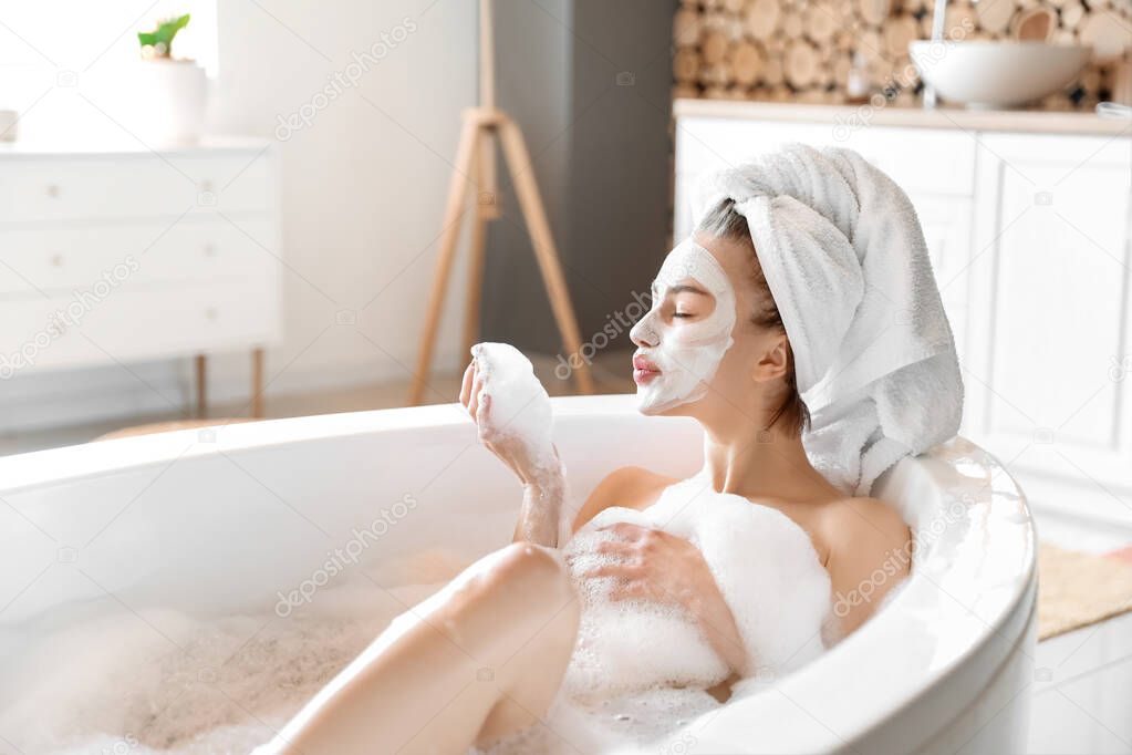 Young woman with facial mask taking relaxing bath at home