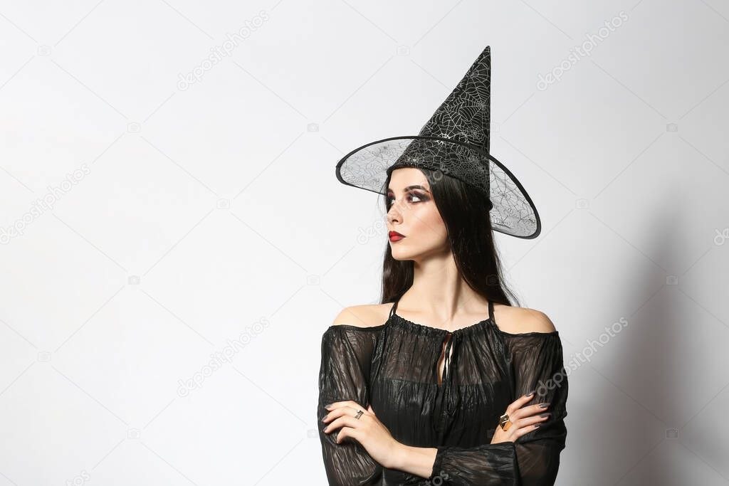 Beautiful woman dressed as witch for Halloween party on light background